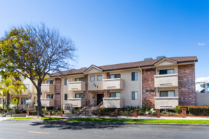 Wide-angle view of Park Providencia Apartments at 725 E Providencia Ave in Burbank, showing red brick exterior, balconies, gated entry, and tree-lined street