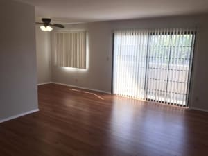 Spacious Burbank apartment living room with hardwood-style floors, vertical blinds, and a ceiling fan.